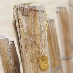 Colliers en chaîne dorée avec pendentif perle et gravure, exposés sur un poteau en bois boutique.