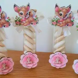 Quatre tubes transparents remplis de bonbons blancs, décorés de cerfs et fleurs roses, posés sur bois.