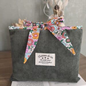 Pochette en velours vert avec ruban fleuri et étiquette française sur un livre ouvert, accessoire élégant.