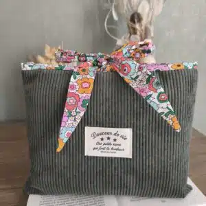 Pochette en velours vert avec ruban fleuri et étiquette française sur un livre ouvert, accessoire élégant.