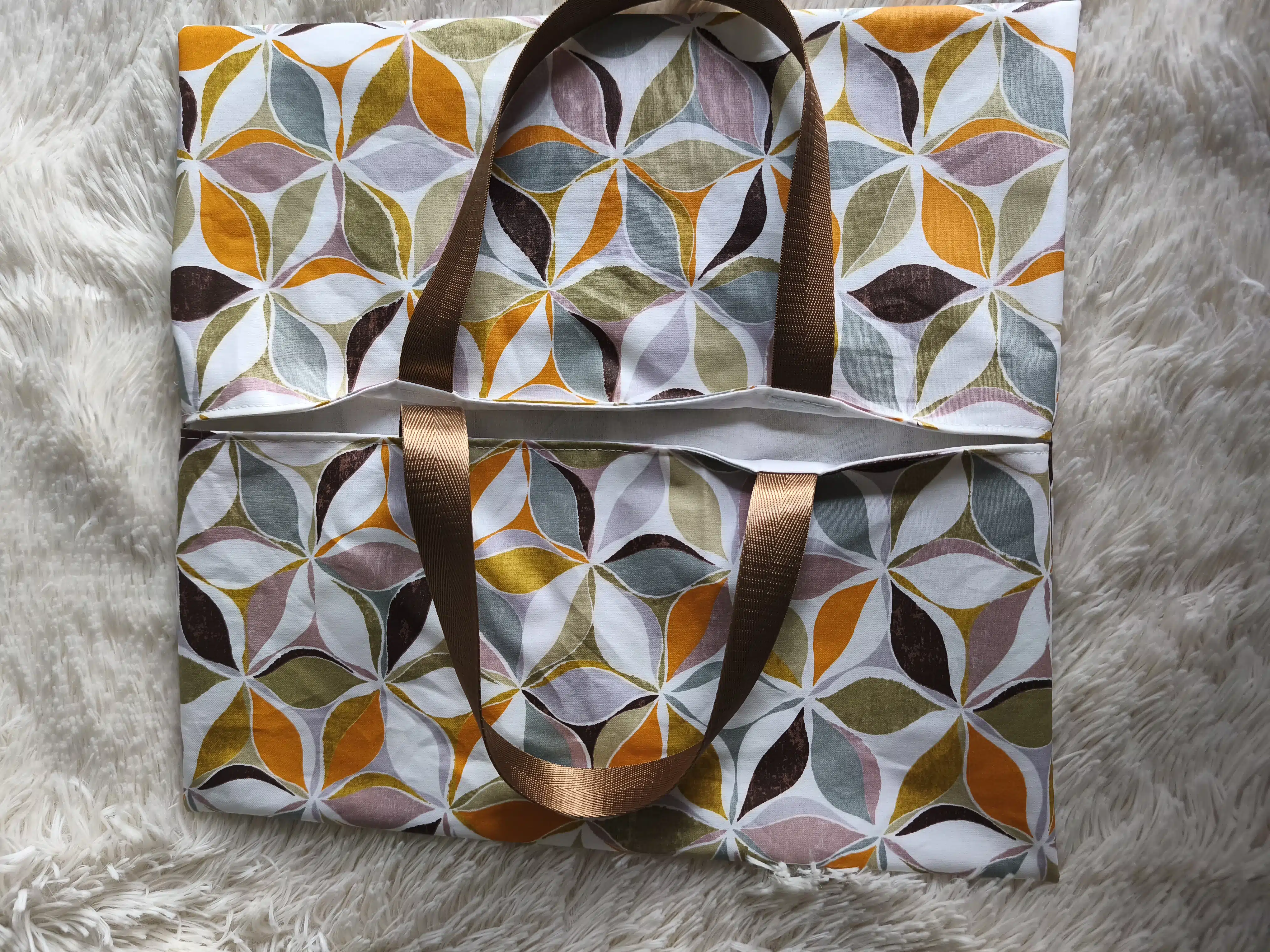 Sac à tarte 5 Sac cabas en tissu motif géométrique multicolore, anses marron, posé sur une surface blanche texturée.