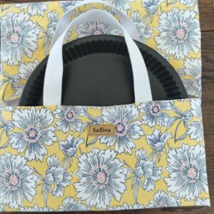 Moule à tarte cannelé partiellement glissé dans un sac en tissu jaune à motif fleuri et anses blanches.
