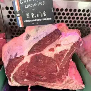Grosse côte de bœuf Limousine crue exposée chez le boucher, étiquette de prix visible, viande fraîche.