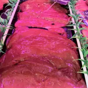 Foie de bœuf cru exposé chez le boucher, décoré de verdure artificielle, pancarte indicative visible.