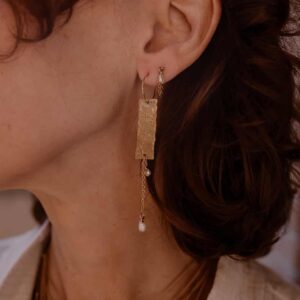 Gros plan sur l'oreille d'une femme avec longue boucle dorée et colliers dorés superposés, haut clair.