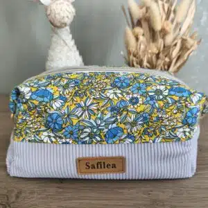 Pochette en tissu fleurie bleu, jaune et blanc Safilea posée sur une surface en bois.