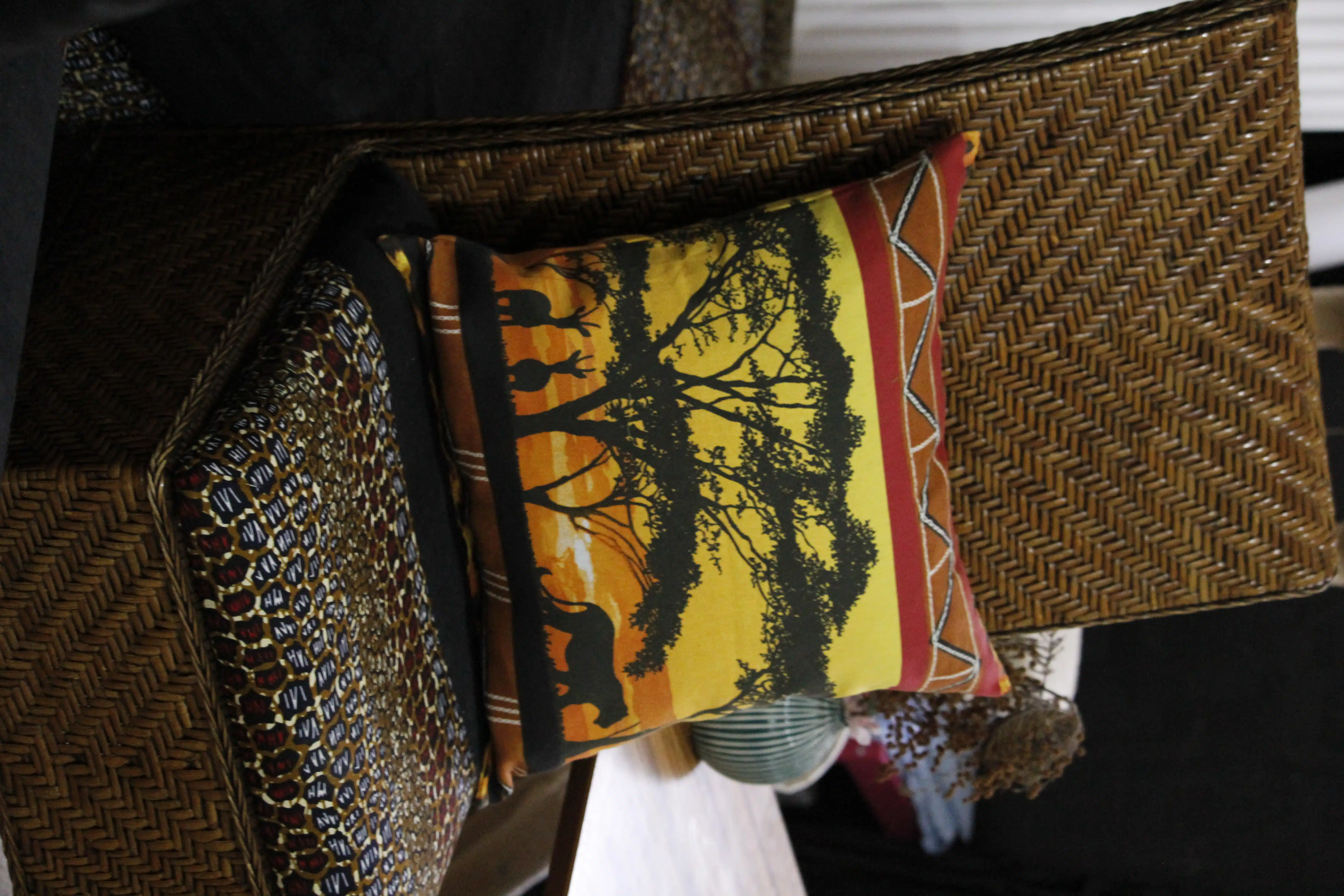 Coussin décoratif « Savane » en toile de coton 3 Chaise tressée avec coussin décoré d'une savane africaine, arbres et silhouettes d'animaux, ambiance exotique.