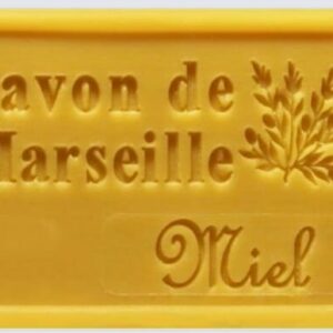 Savon de Marseille Miel jaune, gravé d'une branche, posé sur une surface claire. Savon artisanal naturel.