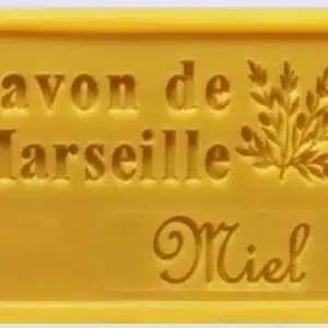 Savon de Marseille Miel jaune, gravé d'une branche, posé sur une surface claire. Savon artisanal naturel.