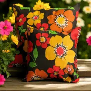 Coussins carrés motifs floraux jaune, orange et rouge posés sur surface en bois à l'extérieur.