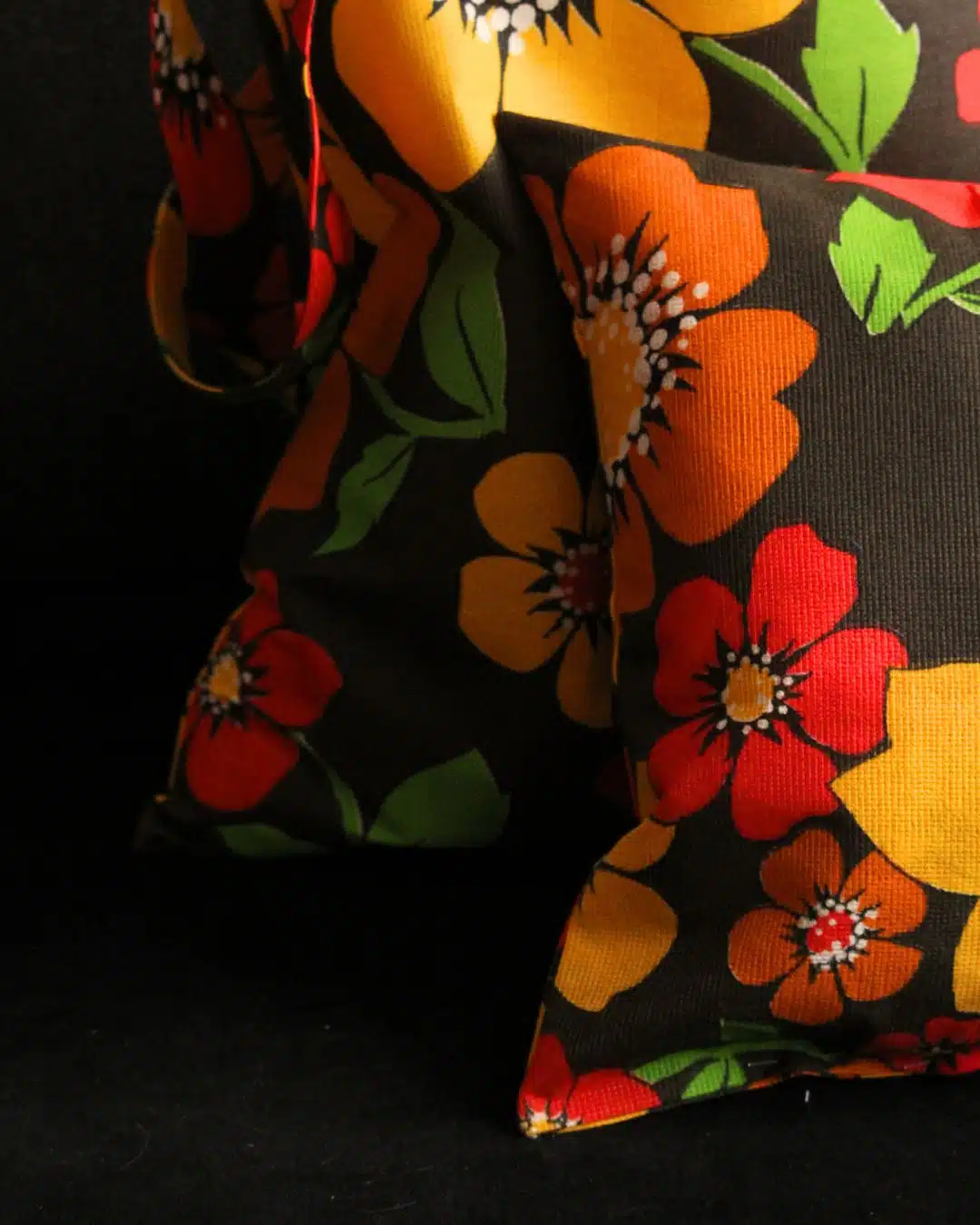 Coussin floral multicolore extérieur 3 Deux coussins motif floral coloré rouge, jaune, orange sur fond sombre, décoration intérieure tendance.