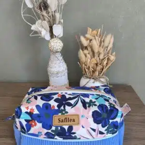 Pochette en tissu bleue à fleurs Safilea sur bois, près de deux vases de plantes séchées.