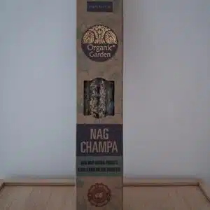Boîte d’encens « Nandita Organic Garden Nag Champa » posée sur un support en bambou, avec un mur blanc en arrière-plan.