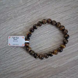 Bracelet composé de perles rondes « œil-de-tigre » de 8 mm, montées sur une base en bois clair, avec étiquette visible.