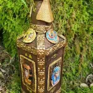 Accueil 13 Bouteille carrée ornée de motifs dorés égyptiens, posée sur de la mousse verte à l'extérieur, dans un style parfum de luxe.