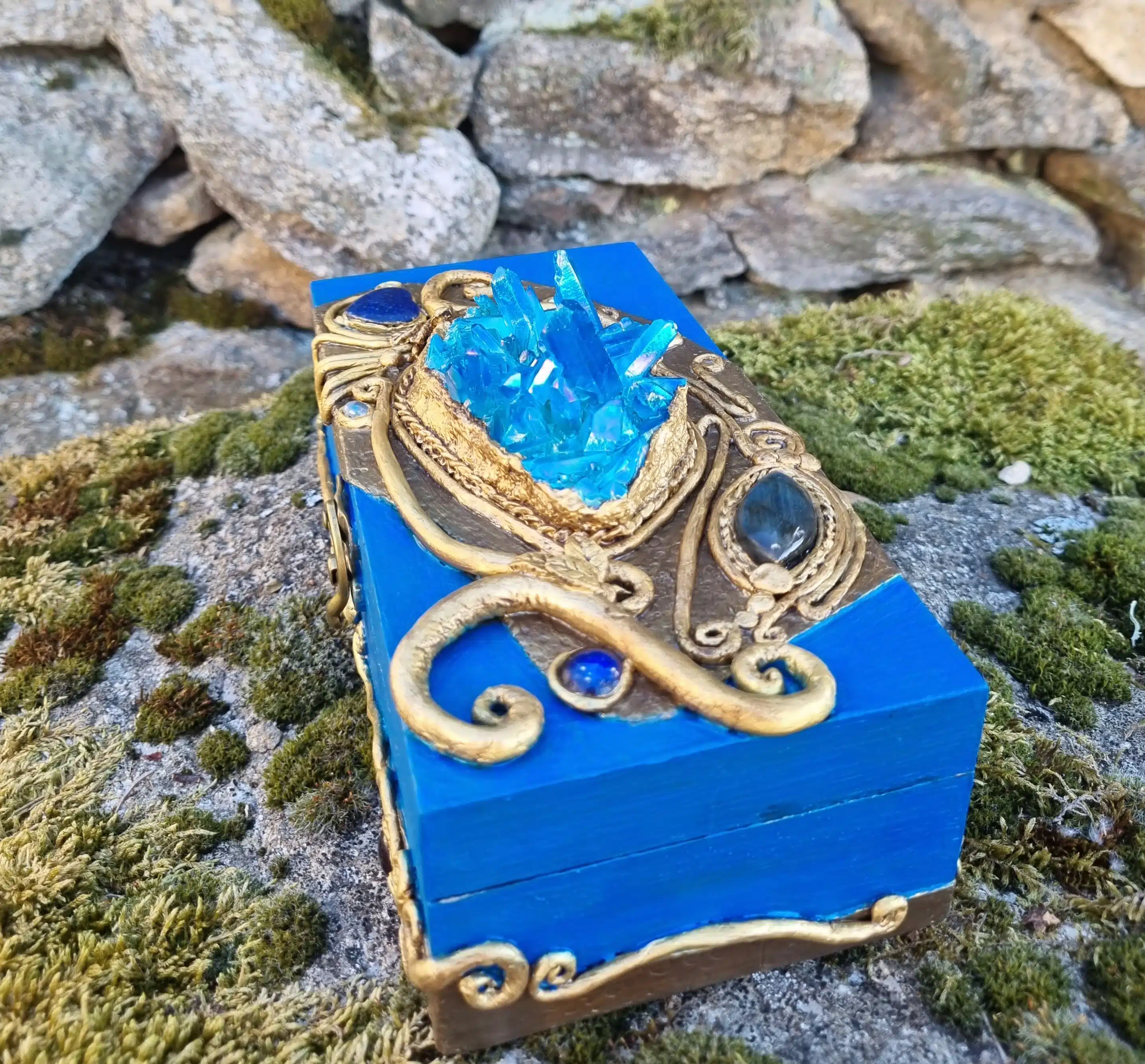 Coffret décoratif bleu & or – Cristaux – Pièce unique artisanale 4 Boîte en bois bleu ornée de dorures et de cristaux, posée sur une pierre et de la mousse verte naturelle.