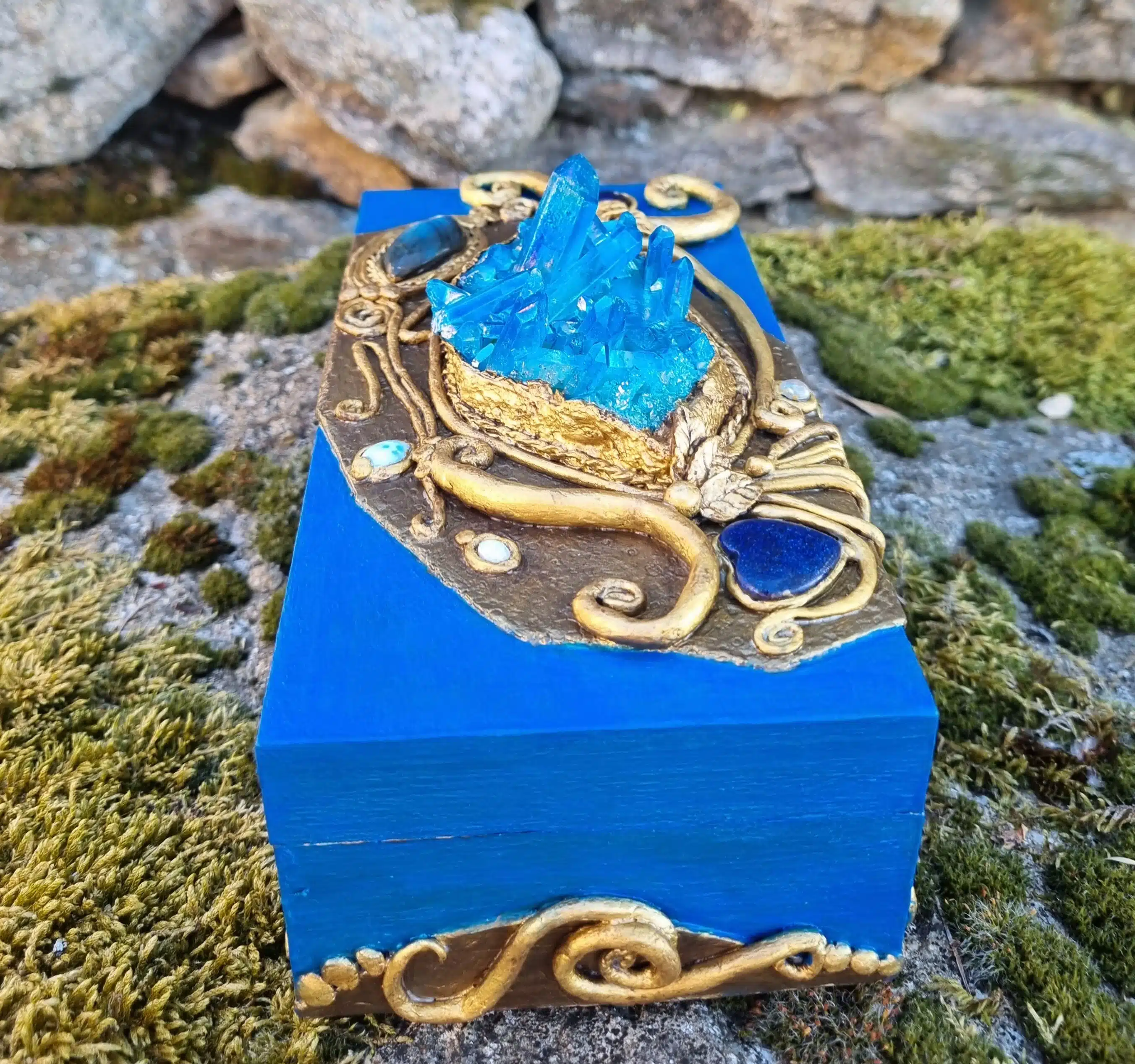 Coffret décoratif bleu & or – Cristaux – Pièce unique artisanale 7 Boîte bleue aux bordures dorées et ornée de cristaux, posée sur de la mousse près de pierres naturelles.