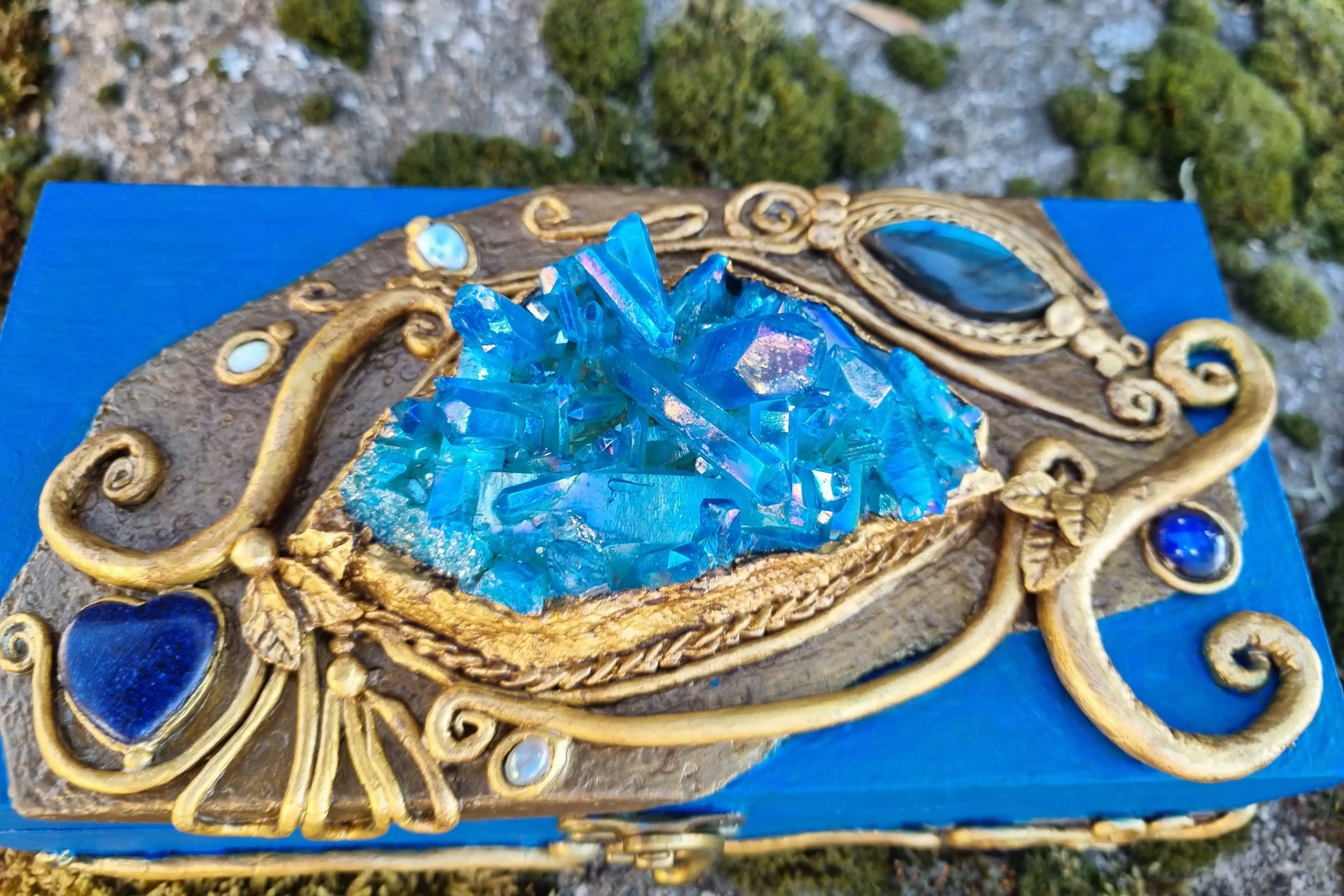 Coffret décoratif bleu & or – Cristaux – Pièce unique artisanale 9 Ensemble de cristaux bleus posé sur une boîte dorée et bleue, avec de la mousse et des pierres en arrière-plan.