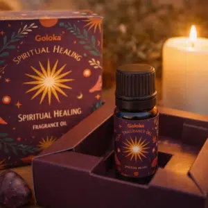 Flacon d’huile parfumée Goloka Spiritual Healing dans son coffret, près d’une bougie allumée.