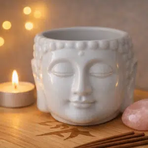 Jardinière en forme de tête de Bouddha en céramique blanche, avec un plateau en bois, une bougie et une pierre décorative.