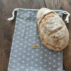 Accueil 9 Pain au levain croustillant posé sur un sac en tissu à motifs géométriques, table en bois.