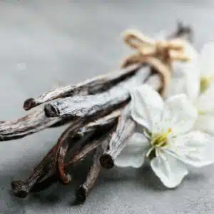 Gousses de vanille séchées, attachées avec de la ficelle, accompagnées de fleurs blanches.